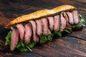 Grilled baguette steak sandwich with arugula and cheese. Dark wooden background. Top view