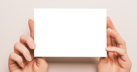 Female hands hold a blank sheet of paper on a beige background. Advertising space