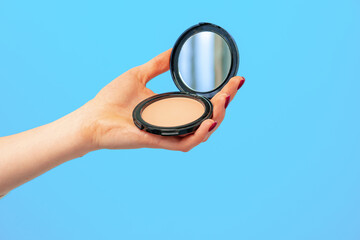 Female hand holding compact powder against blue background