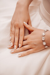 Beautiful well-groomed female hands on the background of a white dress 
