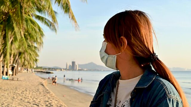 happy young woman with protect face mask travel at the beach and sunset sky on the beach in Thailand,Summer concept travel new normal
