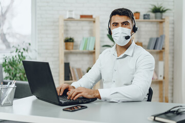 Fototapeta na wymiar Young businessman sitting at his working desk with medical mask on