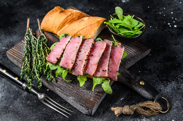 Baguette Tuna steak sandwich with arugula on a cutting board. Black background. Top view