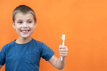 Boy without milk upper tooth in blue t-shirt holds toothbrush in hand on the orange background. Copy space.