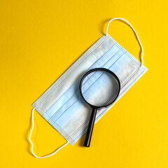 Covid-19 concept. Protective mask through magnifying glass on yellow background