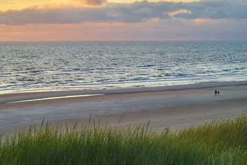 two people can be seen far away on the beach in Vejers Strand (Denmark) during a beautiful sunset over the North Sea