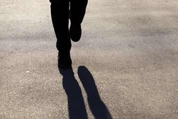 Silhouette of person running the street, runner shadow on pavement. Woman in sneakers runs on sidewalk, concept for jogging, healthy lifestyle