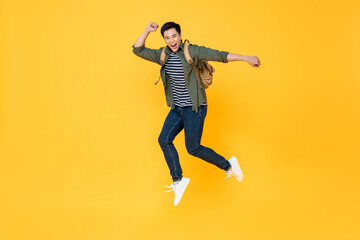 Fototapeta na wymiar Happy smiling young Asian tourist man with backpack jumping in mid-air isolated on yellow background