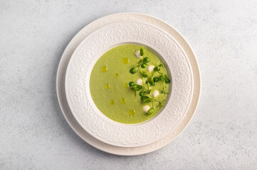 Homemade soup puree of green peas, coconut milk with mini mozzarella cheese in white plate on light background, top view