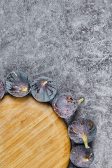 Purple figs around a wooden plate on a marble background