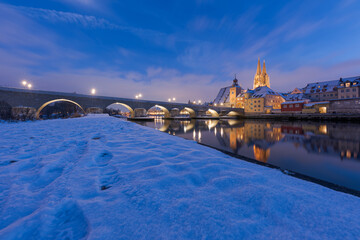 Cathedral, stone bridge and old town of Regensburg on the danube river in winter with fresh snow