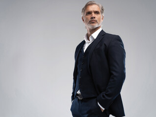 Handsome middle-aged man in suit posing against grey background