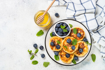 Cottage cheese pancakes, syrniki with blueberry in craft plate. Top view on white stone table with copy space.