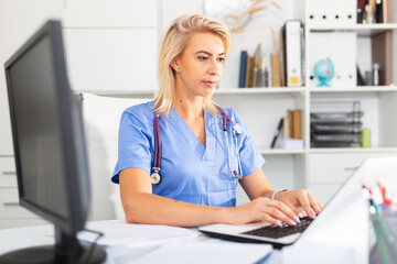 Woman doctor sitting at workplace with computer in her office