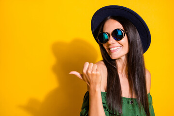 Photo portrait of cute woman pointing thumb at blank space behind shoulder isolated on vivid yellow colored background