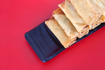 A plate of fried spring rolls at the beginning of spring on a red background