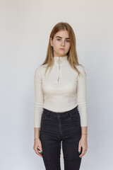 portrait of cute thoughtful teen model wearing white sweater and black jeans. caucasian skinny young female with blond hair isolated on white background. natural pretty lady stands at studio