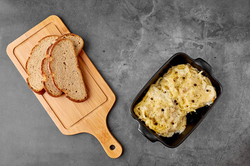 Nest of spaghetti on a baking plate, stuffed with chicken fillet with cheese on a gray textured background top view. next to it is a cutting board with a slice of bread. Food menu