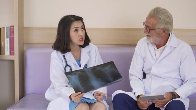 Caucasian and Asian male and female doctor talk and discuss with x-ray image in hospital. New normal lifestyle concept to prevent spread of Covid-19 Coronavirus 