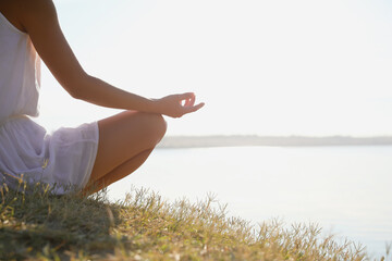 Young woman meditating near river at sunset, closeup view with space for text. Nature healing power
