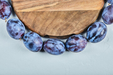 Group of fresh plums around the wooden plate