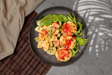 Color Farfalle ready-made pasta with chicken cutlets with herbs and tomatoes. A variety of types and forms of Italian pasta. pasta in the form of bows in a round plate on a gray background, top view