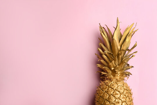 Top view of painted golden pineapple on pink background, space for text. Creative concept