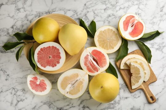 Fresh cut and whole pomelo fruits with leaves on white marble table, flat lay