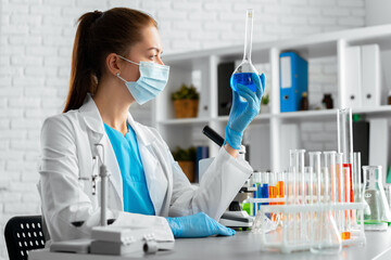 Woman scientist or laboratory worker holding glass flask with chemical liquid