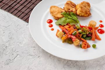stewed vegetables with herbs and chicken steaks in batter on a white plate with drops of ketchup on a gray concrete background top view, food menu with a place to copy the text