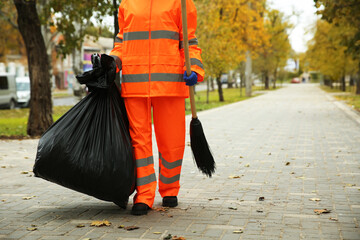 Street cleaner with broom and garbage bag outdoors on autumn day, closeup