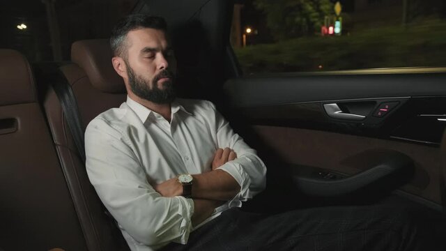 Medium shot of tired adult businessman napping at backseat of taxi while driving home at night