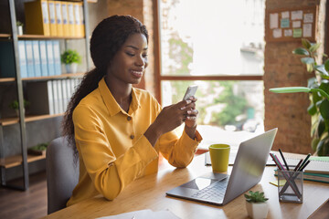 Photo portrait of african american girl texting on phone at workplace in modern office indoors