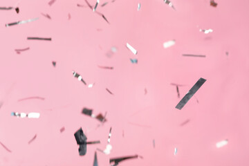 Shiny silver confetti falling down on pink background