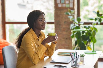 Profile side photo of happy afro american business woman look sit desk take coffee break indoors in...