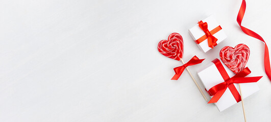 Valentines day banner - white gift boxes with red silk bow, ribbon, lollipops hearts on white wood table, copy space.