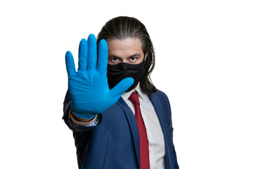 A man in a business suit, in a protective mask and gloves, shows a stop on a white background. Selective focusing. 