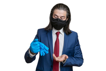 A young man in a business suit, in a protective mask, takes off medical gloves from his hands on a white background. The manager takes off his gloves after a working day.