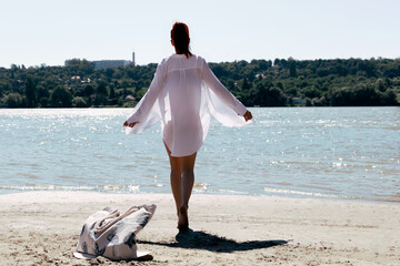 Rear view of woman in white shirt walking down the beach.