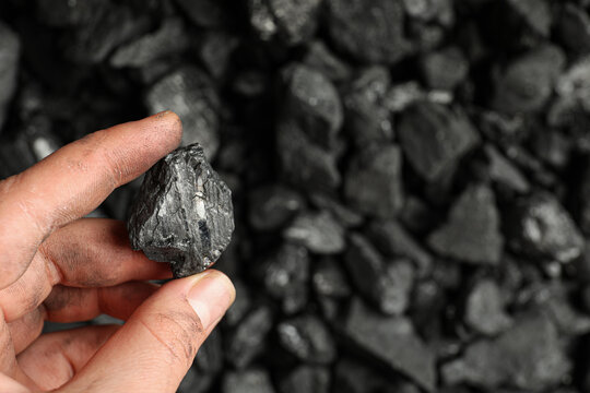 Man holding piece of coal over pile, closeup. Space for text