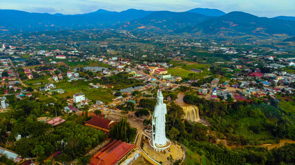 Fototapeta na wymiar Aerial view of Linh An Pagoda, DaLat city, Lam Dong province, Vietnam. A statue is white and 71 meters high. Selective focus. Thac Voi waterfall, forest and city scene in background.