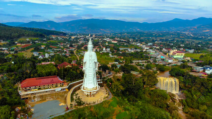 Fototapeta na wymiar Aerial view of Linh An Pagoda, DaLat city, Lam Dong province, Vietnam. A statue is white and 71 meters high. Selective focus. Thac Voi waterfall, forest and city scene in background.