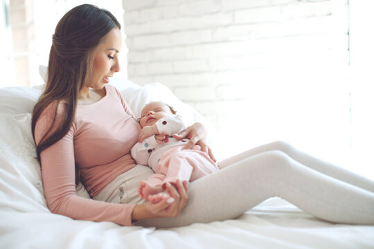 A loving mother caring for her newborn baby at home. Bright portrait of a happy mother holding a sleeping baby in her arms. High quality photo.