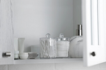 Fototapeta na wymiar Cotton buds and pads in transparent holders near toiletries on shelf