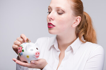 Fototapeta na wymiar red-haired woman putting a coin into her piggy bank