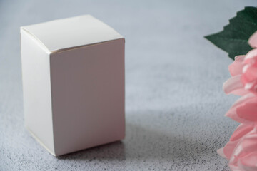 White box on a gray background with pink dahlia flower in a corner. Product concept