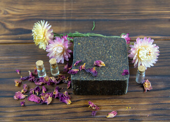 Handmade soap-scrub, decorated with dried flowers, lies on the brown wooden countertop.