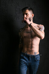Portrait of a brutal beard gentleman with tattoo body smoking cigar in hot elegant suit shirtless man naked in loft apartment . Strong confident tattooed male smoke