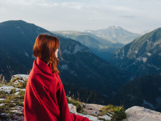 red-haired woman with a plaid on her shoulders are resting in the mountains