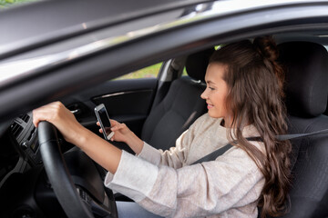Plakat safety and people concept - happy smiling young woman or female driver with smartphone driving car in city